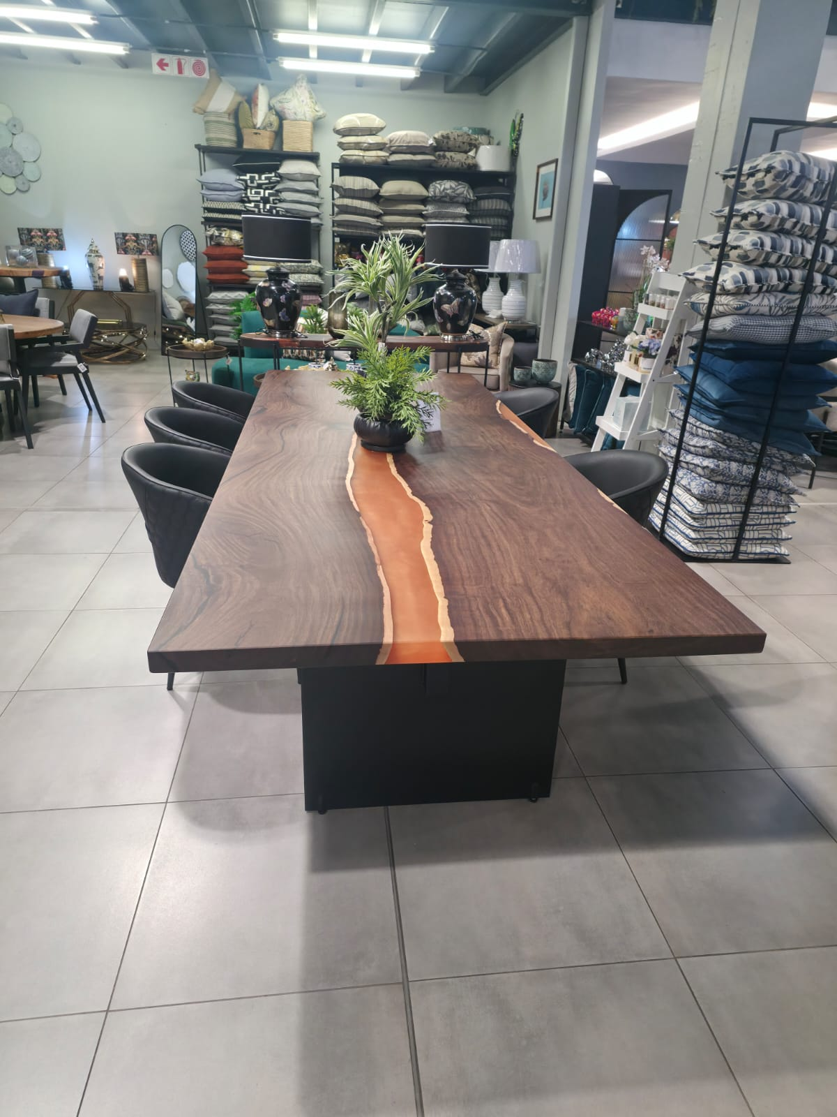 Walnut dining table with a warm amber resin river on a black plinth base