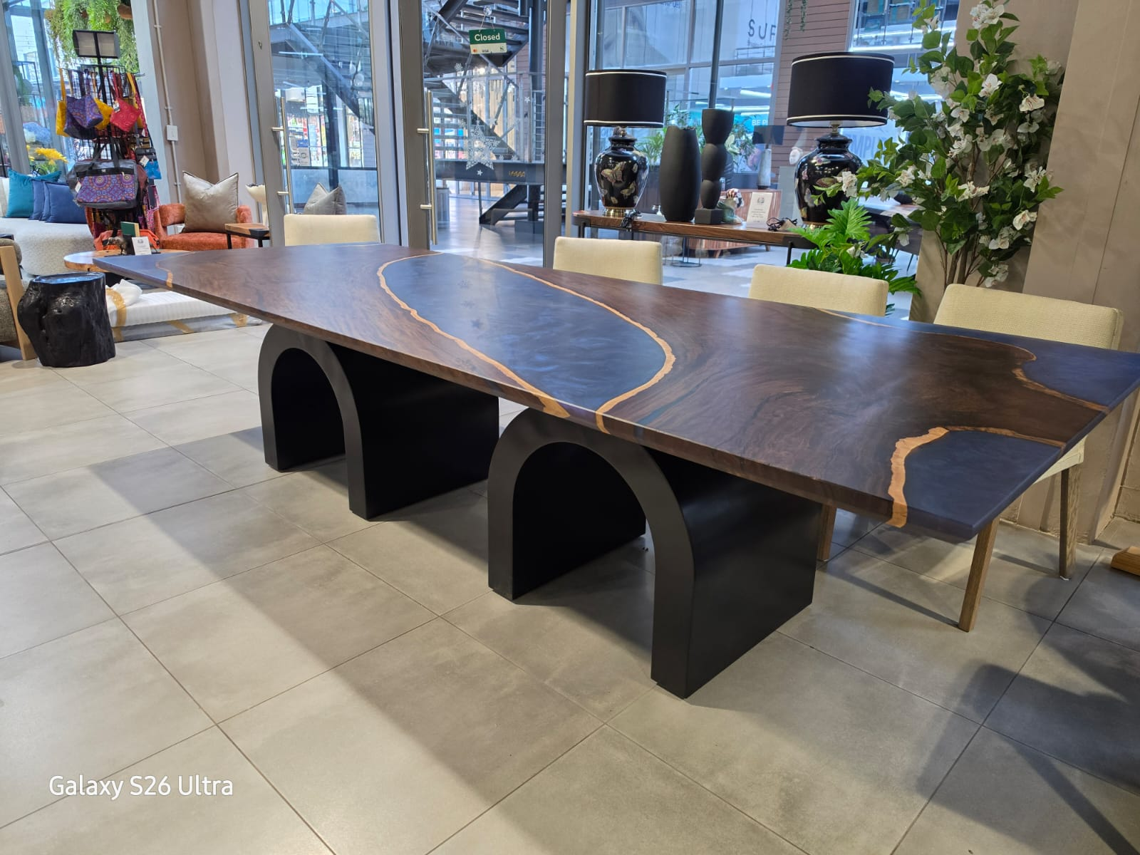 Live-edge wood and resin dining table in dark walnut with a smoke resin river on arched steel bases
