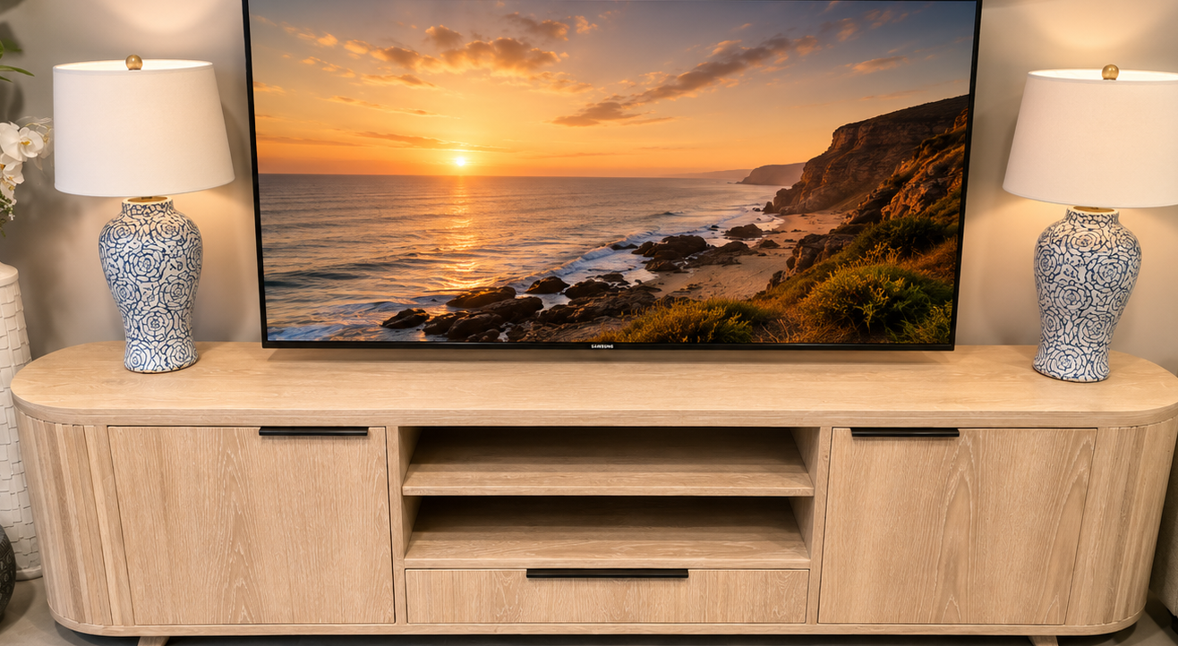 TV on a wooden stand with sunset over ocean scene, flanked by two lamps in a living room.